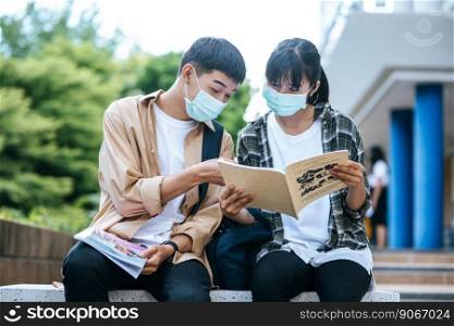Male and female students wearing masks sit and read books on the stairs