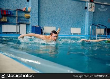 Male and female swimmers swims in the pool. Man and woman in the water, sport swimming skill training, motion view, workout before competition. Male and female swimmers swims in the pool