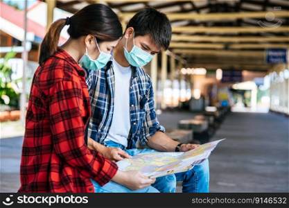 Male and female tourists look at the map beside the railway.