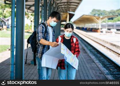 Male and female tourists look at the map beside the railway tracks.