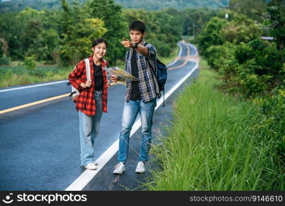 Male and female tourists look at the map on the road.