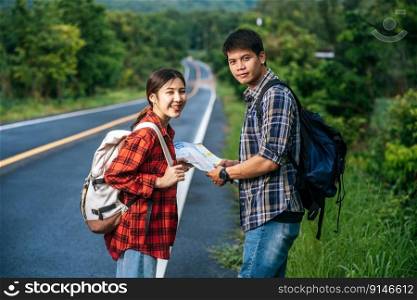 Male and female tourists look at the map on the road.