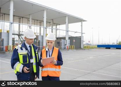 Male and female workers discussing over clipboard in shipping yard