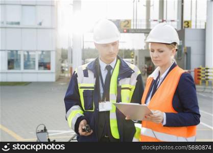 Male and female workers discussing over clipboard in shipping yard