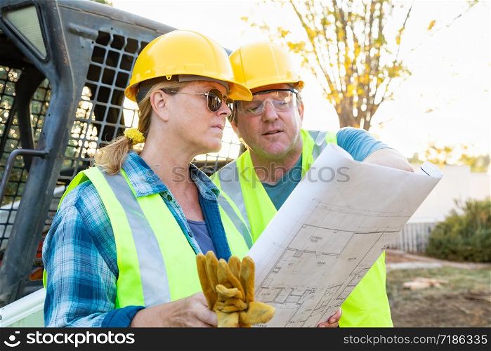 Male and Female Workers With Technical Blueprints Talking at Construction Site
