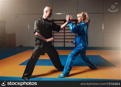 Male and female wushu fighters exercises indoor, martial arts. Sparring partners in action. Male and female wushu fighters exercises indoor