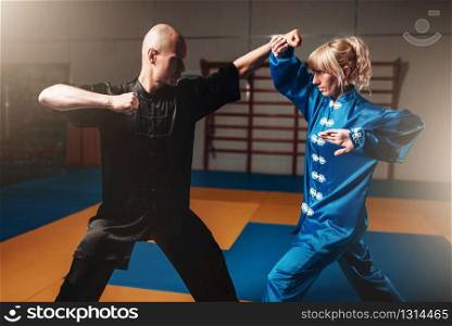 Male and female wushu fighters exercises indoor, martial arts. Sparring partners in action. Male and female wushu fighters exercises indoor