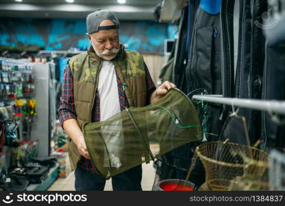 Male angler choosing net in fishing shop, hooks and baubles on background. Equipment and tools for fish catching and hunting, accessory choice on showcase in store, bait assortment. Male angler choosing net in fishing shop