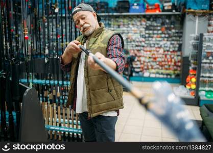 Male angler choosing rod in fishing shop. Equipment and tools for fish catching and hunting, accessory choice on showcase in store, spinnings and telescopes assortment. Male angler choosing rod in fishing shop