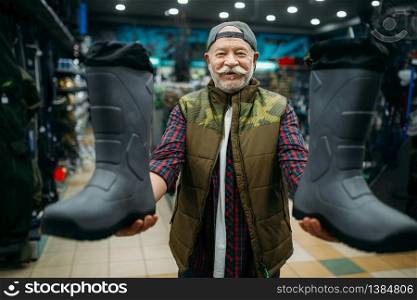 Male angler choosing rubber boots in fishing shop. Equipment and tools for fish catching and hunting. Male angler choosing rubber boots in fishing shop