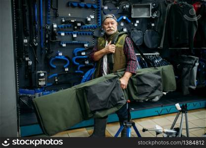 Male angler holds big case for fishing-rods in fishing shop. Equipment and tools for fish catching and hunting, accessory choice on showcase in store. Angler holds case for fishing-rods in fishing shop
