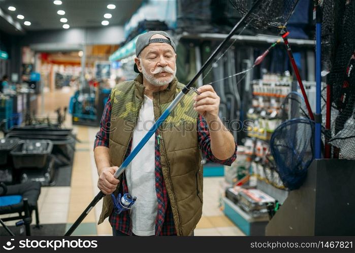 Male angler puts the line in the eye of the rod in fishing shop. Equipment and tools for fish catching and hunting, accessory choice on showcase in store. Angler puts line in the eye of rod, fishing shop