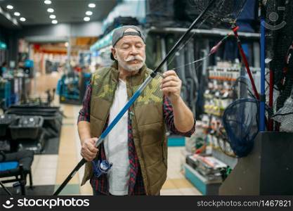 Male angler puts the line in the eye of the rod in fishing shop. Equipment and tools for fish catching and hunting, accessory choice on showcase in store. Angler puts line in the eye of rod, fishing shop