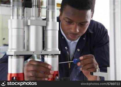 Male Apprentice Engineer Working On Machine In Factory