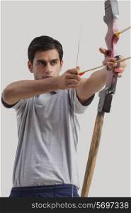 Male archer practicing archery against gray background