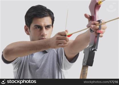 Male archer taking aim with competition bow against gray background
