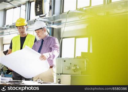 Male architect and manual worker examining blueprint in metal industry