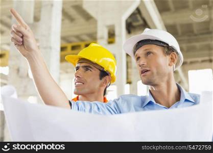 Male architect explaining building plan to colleague at construction site