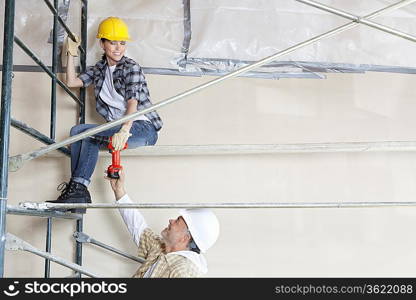 Male architect giving drill to female worker on scaffold at construction site