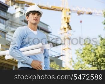 Male architect holding rolled up blueprints while standing at construction site