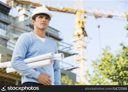 Male architect holding rolled up blueprints while standing at construction site