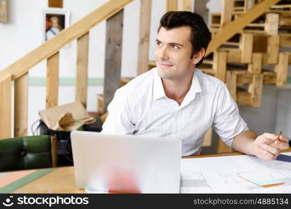 Male architect in office. Male architect with computer studying plans in office