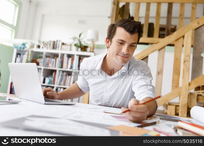 Male architect in office. Male architect with computer studying plans in office