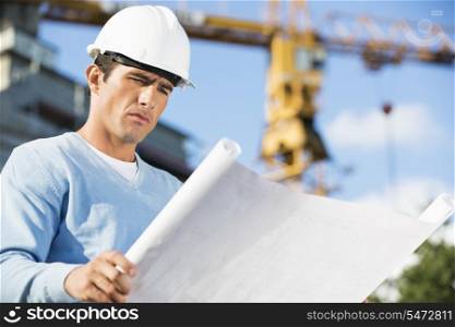 Male architect reviewing blueprint at construction site