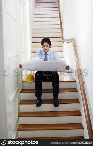 Male architect studying a blueprint on the staircase
