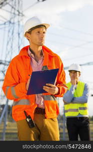 Male architect with clipboard working at site while coworker standing in background