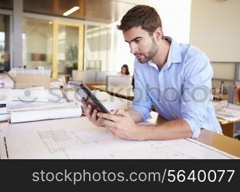 Male Architect With Digital Tablet Studying Plans In Office