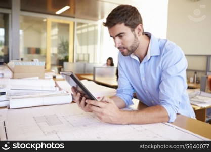 Male Architect With Digital Tablet Studying Plans In Office