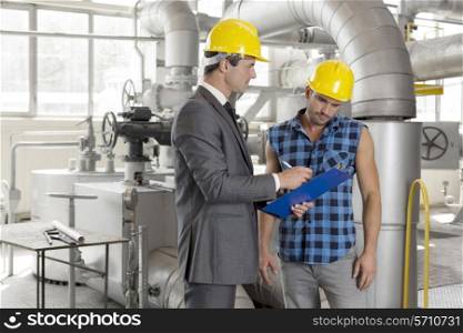 Male architect with worker discussing over clipboard in industry