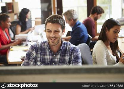 Male Architect Working At Desk With Meeting In Background