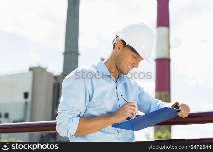 Male architect writing on clipboard at site