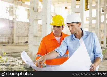 Male architects discussing over blueprint at construction site