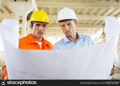 Male architects reviewing blueprint at construction site