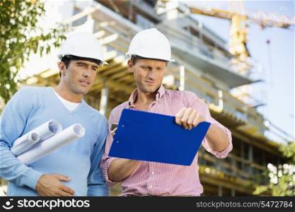 Male architects with blueprint and clipboard working at site