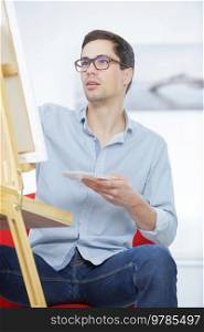 male artist paints on an easel in the workshop