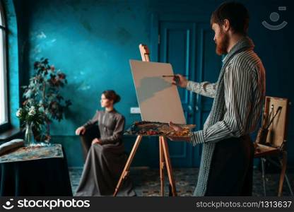 Male artist with palette and brush in hand in front of easel. Oil paint. Artist with palette and brush in front of easel