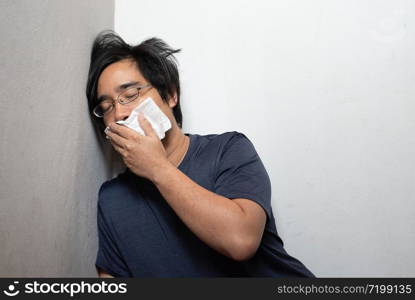 Male Asian young man wearing surgical mask feeling sick headache and coughing leaning on wall isolated on white background.Wuhan coronavirus (COVID-19) outbreak prevention. Health care concept