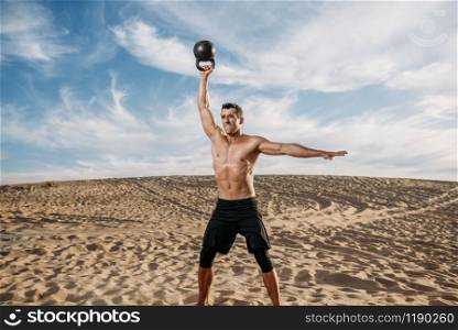 Male athlete doing exercises with weights in desert at sunny day. Strong motivation in sport, strength outdoor training