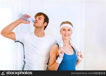 Male athlete drinking water from bottle and smiling girl in sportswear with towel&#xA;
