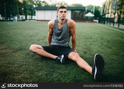 Male athlete on outdoor fitness workout. Sportsman sits on grass and doing stretching exercise. Male athlete on outdoor fitness workout
