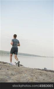 Male athlete/runner running on beach - jog workout well-being concept. Behind view