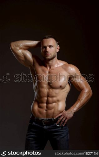 Male athlete with muscular body poses in studio, dark background. One man with athletic build, shirtless sportsman in jeans pants, active healthy lifestyle. Male athlete with muscular body poses in studio