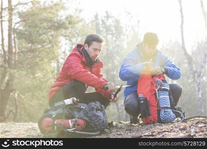 Male backpacker with friend whittling wood in forest