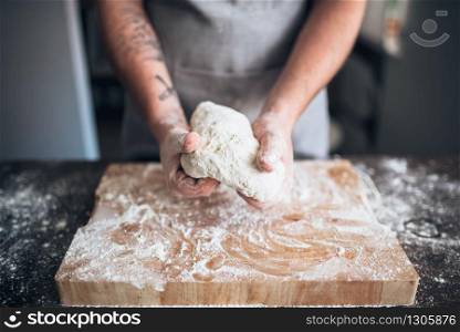 Male baker hands kneading dough on wooden table. Bread preparation. Homemade bakery