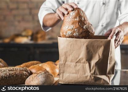 male baker putting baked bread brown paper bag