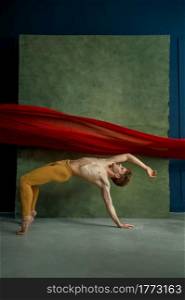 Male ballet dancer doing exercise in dancing studio, grunge wall and red cloth on background. Performer with muscular body, grace and elegance of movements. Male ballet dancer doing exercise, dancing studio